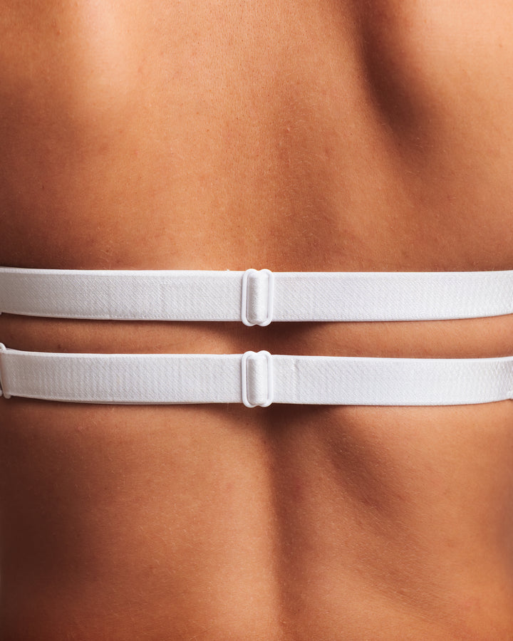 Close-up of a person wearing a white bra against a skin-toned background